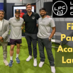 Liam Plunkett with a group of coaches and partners at the launch event of the first LPC Partner Cricket Academy, standing on indoor turf with academy branding in the background.