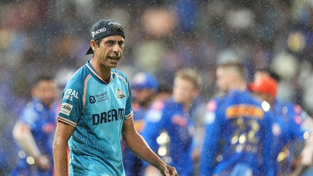 Ashish Nehra, Head Coach of Gujarat Titans, walking on the field during an IPL match in rainy conditions.