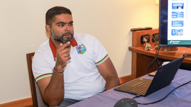 Avenesh Seetaram, Performance Analyst for Cricket West Indies, seated and speaking during a meeting with a laptop and presentation screen.