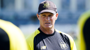 Cricket coach Dale Benkenstein during a training session, wearing team gear and cap, focused on giving instructions.