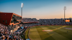 Wide-angle view of Emirates Old Trafford cricket stadium during a packed evening match, with spectators filling the stands under stadium lights.