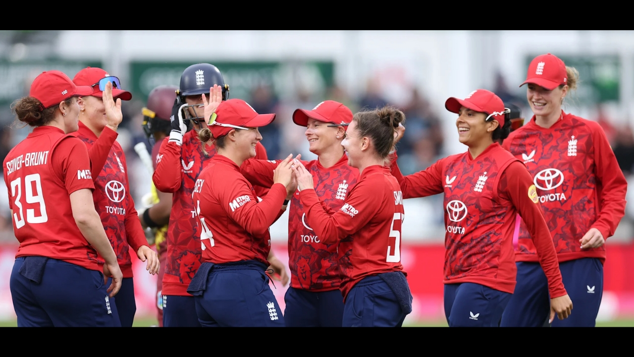 England women's cricket team players celebrating on the field during a match, wearing red and blue kits.