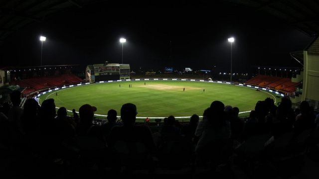 Night view of a cricket match at ExxonMobil Guyana Global Super League with stadium lights and spectators in silhouette