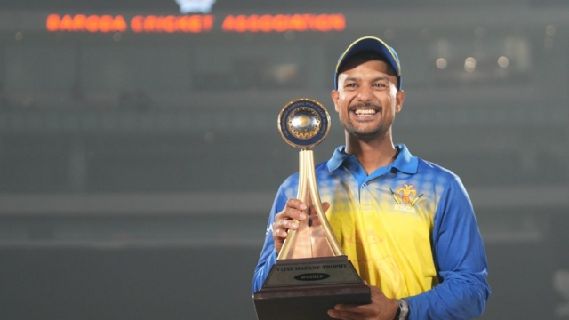 Mayank Agarwal smiling and holding the Vijay Hazare Trophy in Baroda Cricket Association stadium