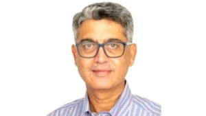 Prathmesh Mishra, Chairman of Royal Challengers Bangalore, wearing glasses and a striped shirt against a white background.