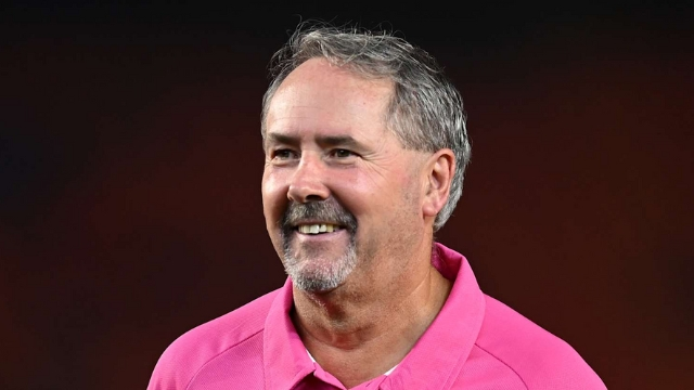 Richard Illingworth, ICC cricket umpire, smiling in a pink shirt against a dark blurred background.