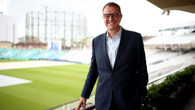 Richard Thompson, ECB chair, smiling and standing at the Oval cricket ground with empty stands and green pitch in the background.
