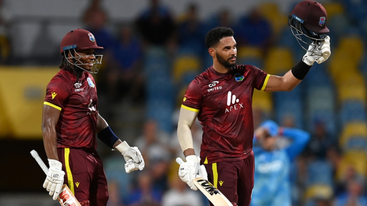 West Indies cricketer Shai Hope raises his helmet and bat in celebration while walking with a teammate during a match.