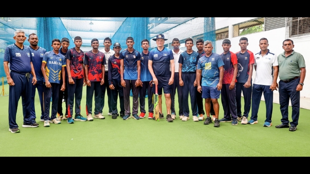 Tim Boon poses with a group of young Sri Lankan cricketers and their coaches during a training session at an indoor cricket facility.