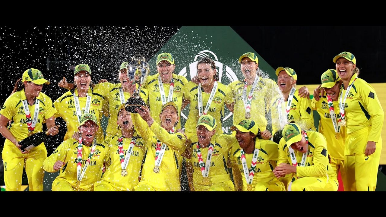 Australia women's cricket team celebrating their World Cup victory with medals and champagne on stage, wearing yellow uniforms and showing jubilation.