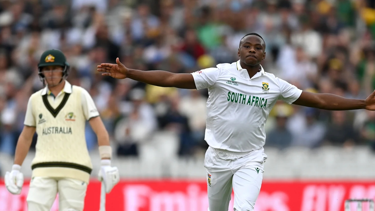 Kagiso Rabada of South Africa celebrates a wicket with arms outstretched during the ICC World Test Championship Final against Australia, with an Australian batter in the background.