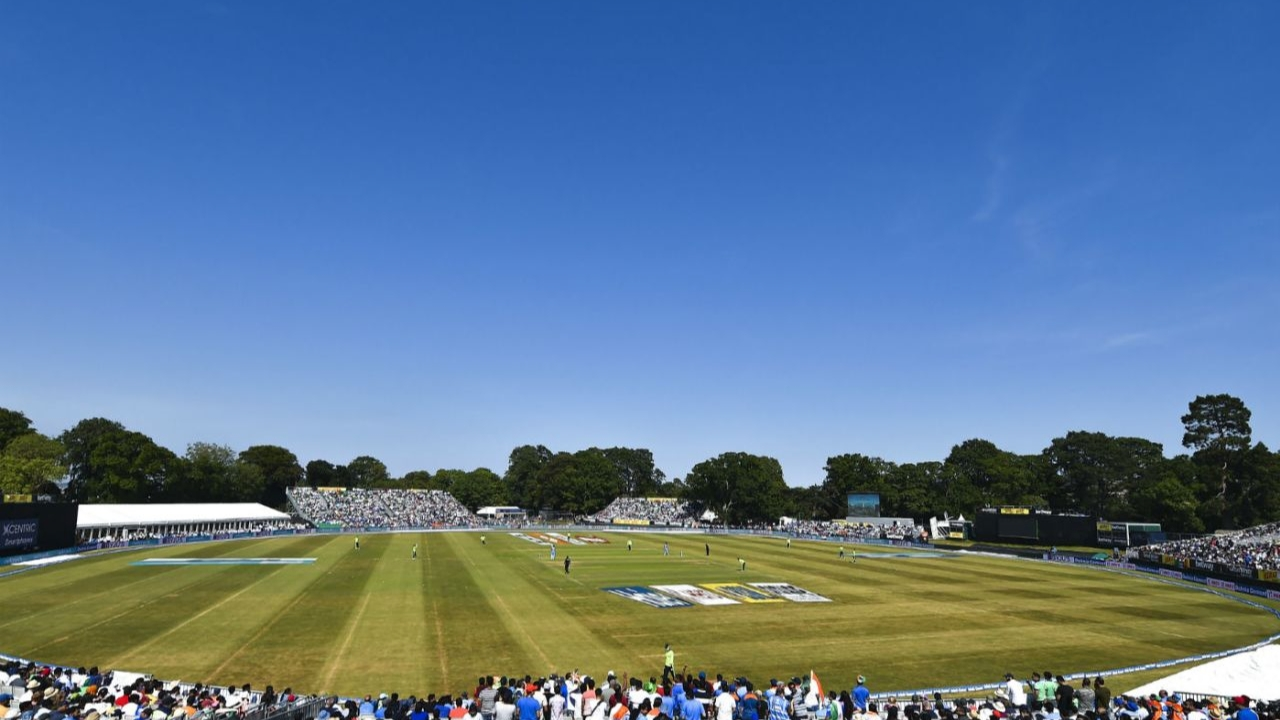 Wide view of Malahide Cricket Ground in Dublin with spectators and players under a clear blue sky.