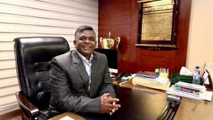 Md Aminul Islam seated at his office desk after being elected as the 17th President of the Bangladesh Cricket Board (BCB), with a plaque and trophy in the background.