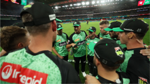 Melbourne Stars cricket team in a huddle wearing green and black jerseys during a Big Bash League match at a packed stadium.