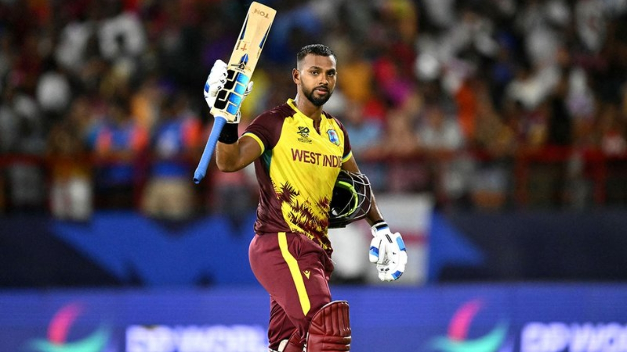 Nicholas Pooran raising his bat to celebrate a milestone while wearing the West Indies T20 jersey during an international cricket match.