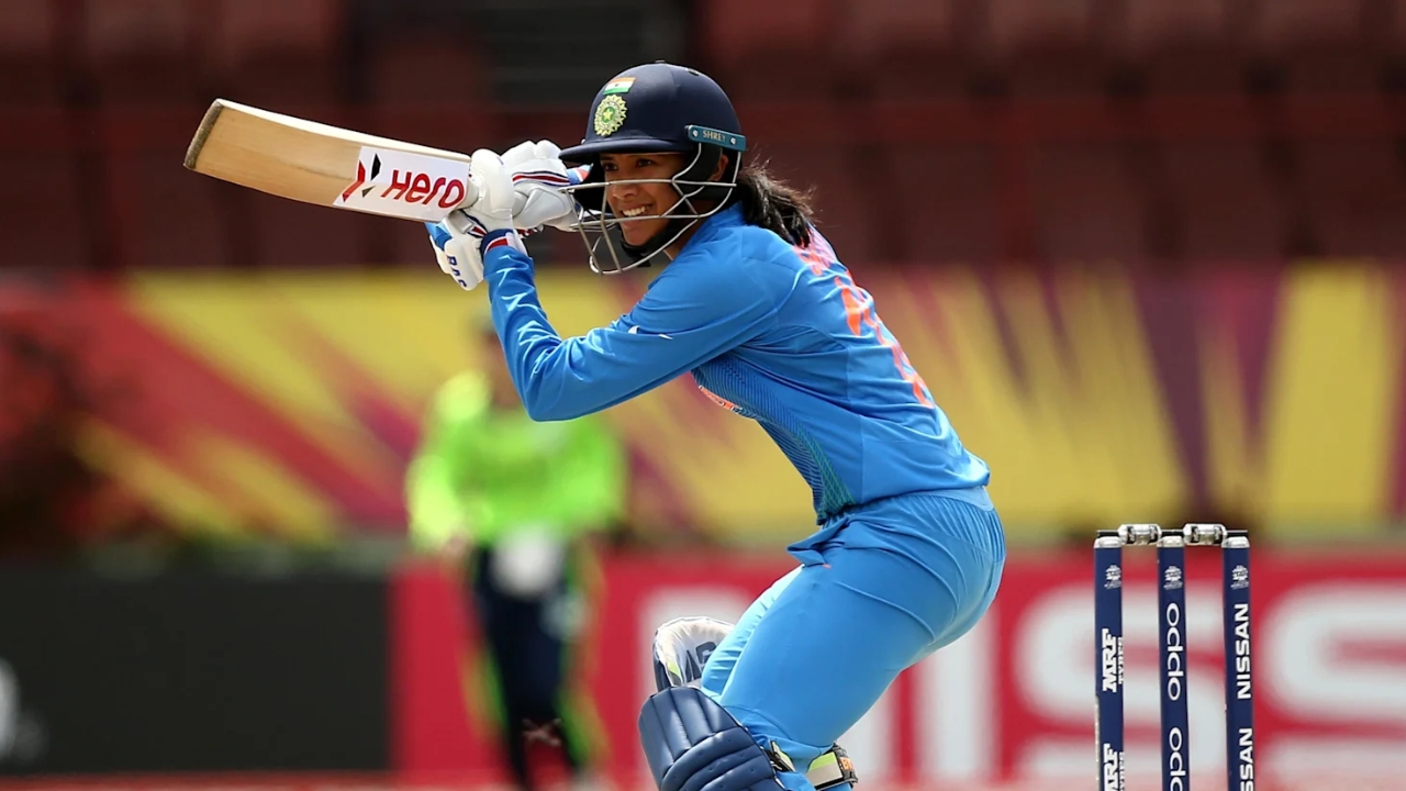Indian cricketer Smriti Mandhana playing a shot during a women's international cricket match, wearing the blue India jersey and helmet.