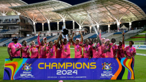 The 2024 Women’s Caribbean Premier League (WCPL) champions celebrating with the trophy, dressed in pink jerseys, standing behind a “Champions 2024” banner at the stadium.