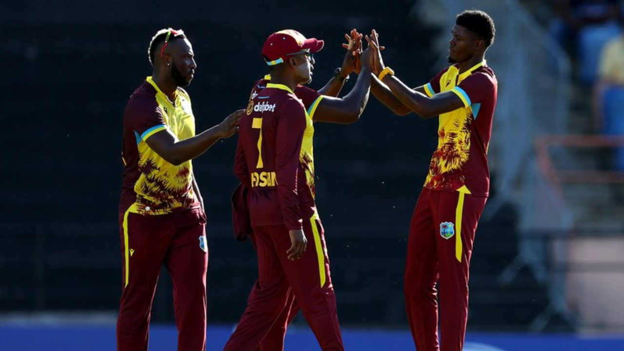 West Indies cricket players in maroon and yellow kits celebrating a wicket with high-fives during a T20 match.