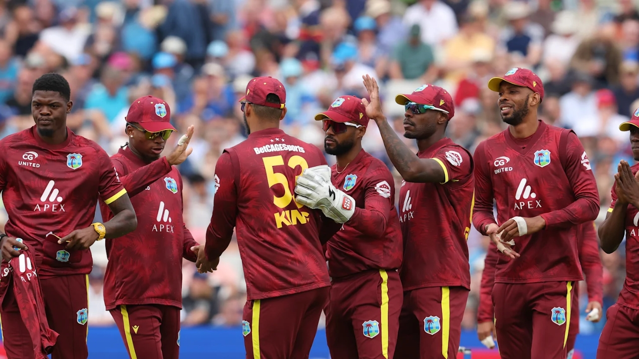 West Indies cricket team players wearing maroon ODI jerseys celebrating during a match, with a crowd in the background.