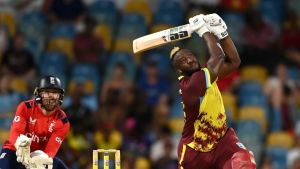 Andre Russell of West Indies plays a powerful shot during a T20 match against England, with Phil Salt keeping wickets behind the stumps.