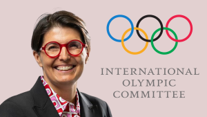 Anne-Sophie Voumard smiling in front of the International Olympic Committee logo with Olympic rings on a light background.