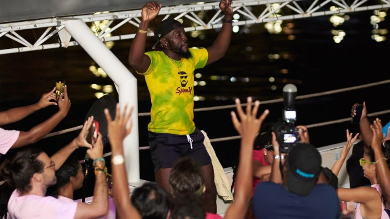 Cricket fan dancing and celebrating on a boat during a Caribbean Premier League (CPL) event at night.