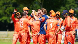 Netherlands men's cricket team wearing bright orange kits celebrating on the field during a match, gathered in a team huddle with high-fives.