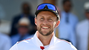 Joe Root smiles during a Test match, wearing England cricket whites and sunglasses.