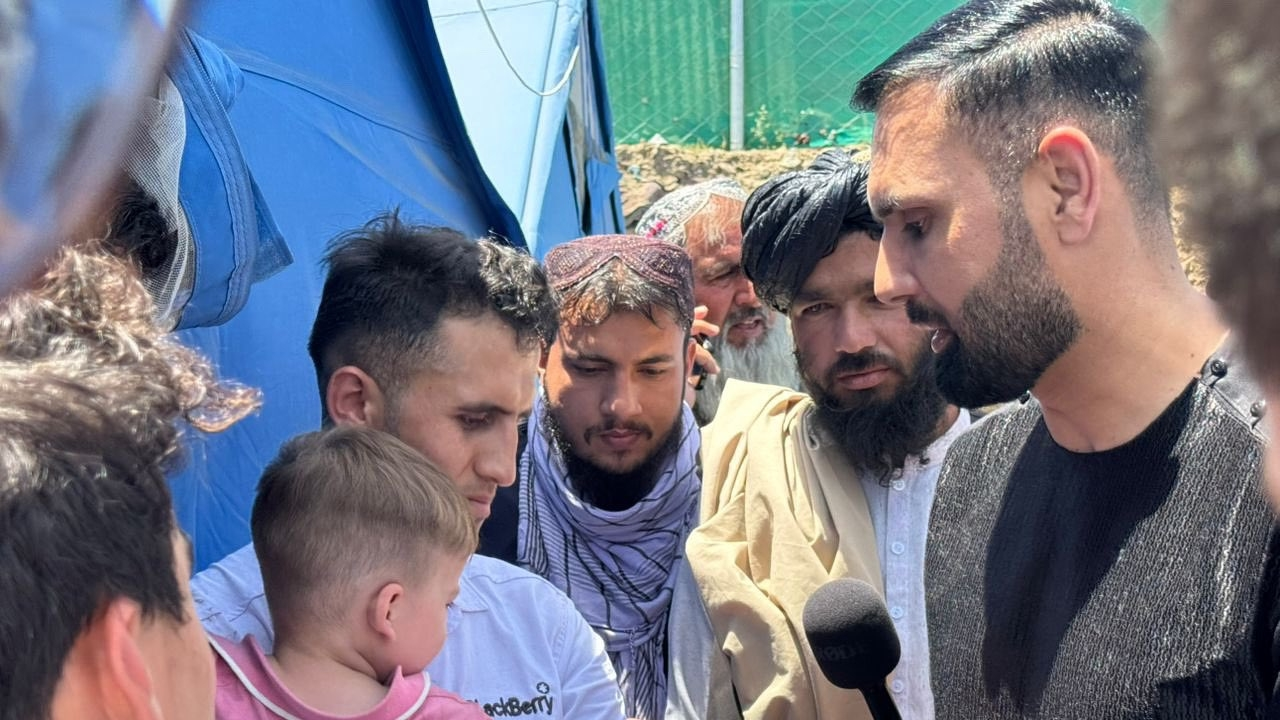 Mohammad Nabi speaking with Afghan returnees during a humanitarian visit, surrounded by men and a child near a tent.