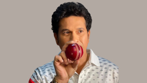 Sachin Tendulkar holding a red cricket ball close to his face while wearing a patterned white shirt.