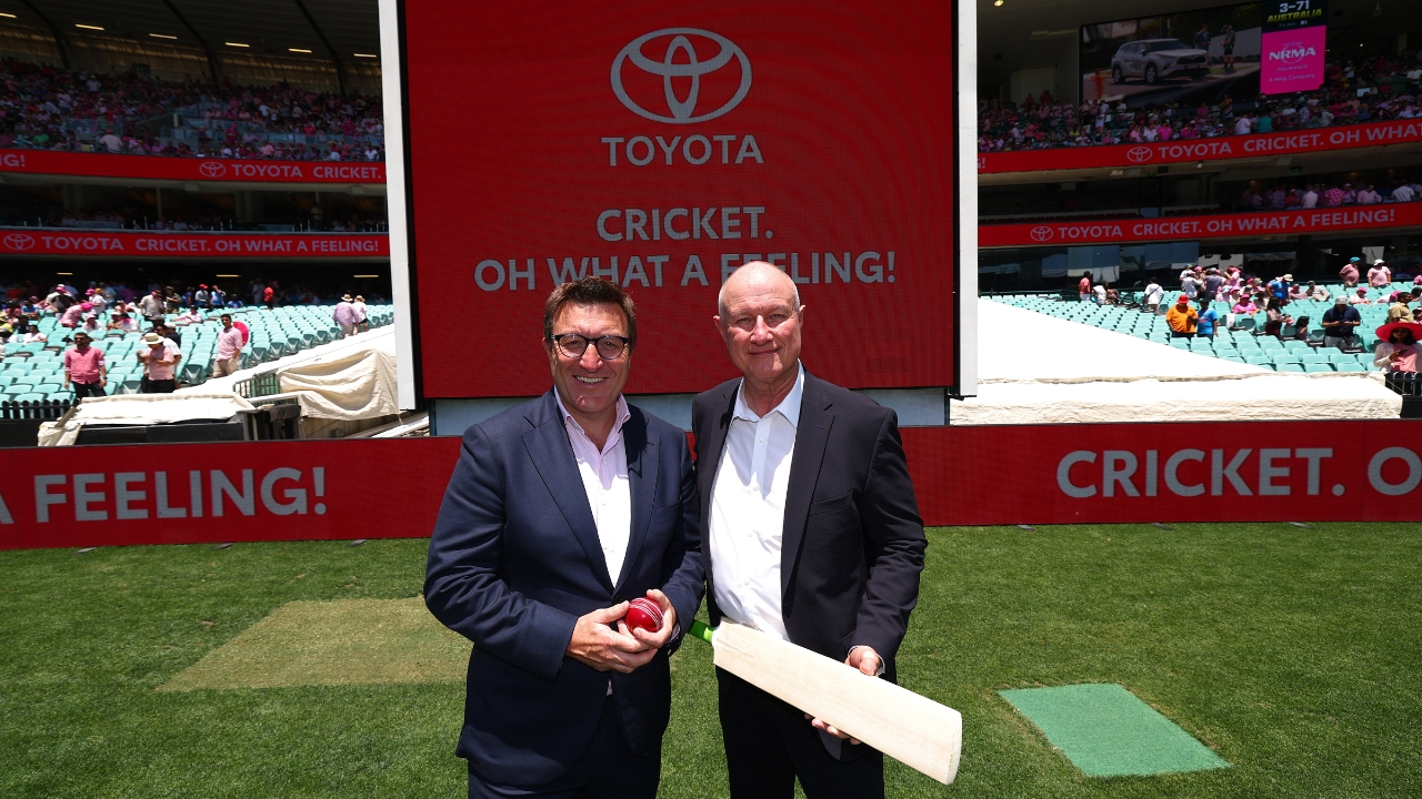 Ed Sanders and Sean Hanley pose on the cricket field during a Toyota sponsorship event at the Sydney Cricket Ground, holding a bat and ball in front of a large Toyota display.