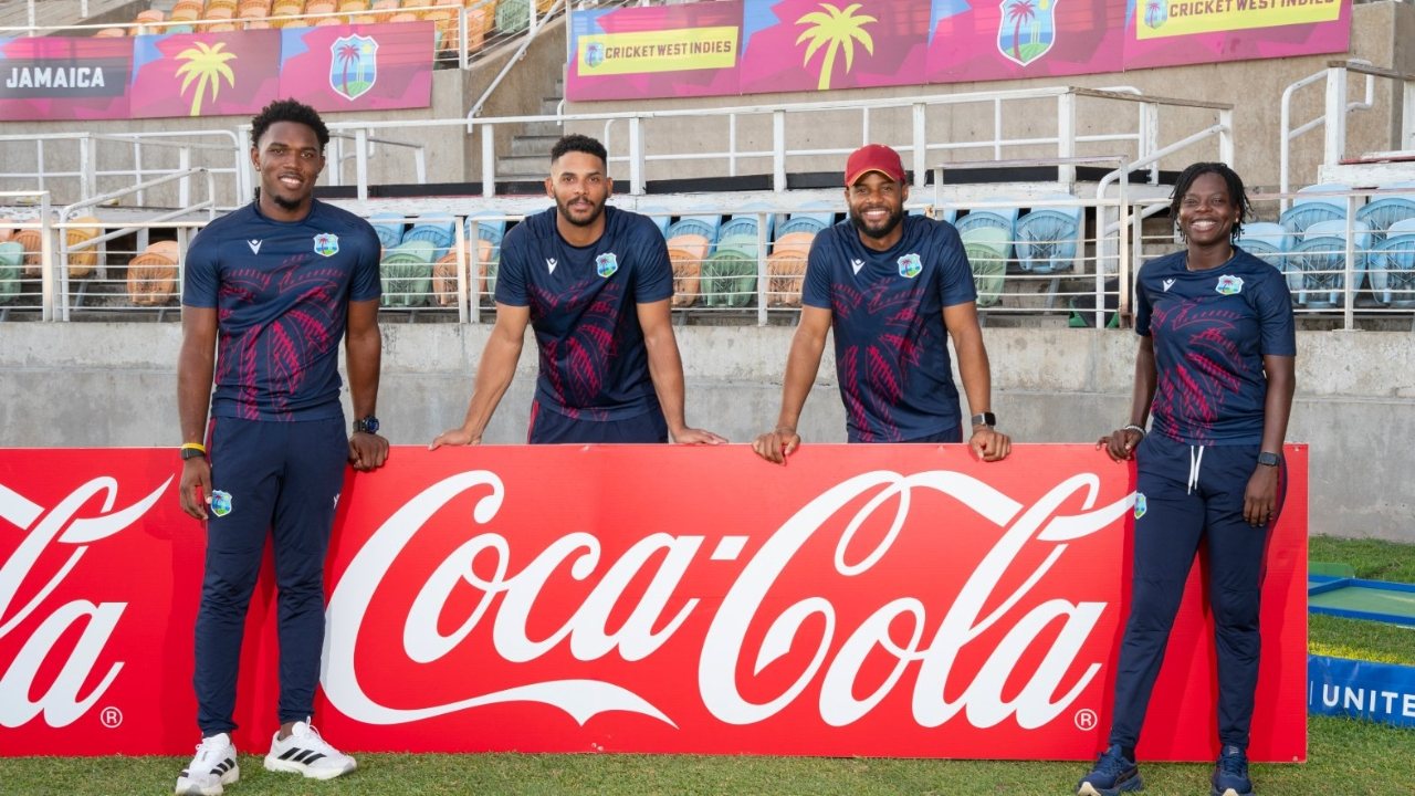 West Indies cricketers posing in front of a Coca-Cola advertising board at a stadium in Jamaica.