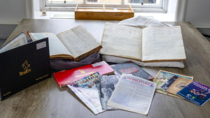 Collection of historic cricket scorebooks, magazines, and newsletters displayed on a wooden table near a window.
