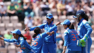 Indian women's cricket team players celebrating on the field wearing their blue ODI jerseys during a match, with a crowd in the background.