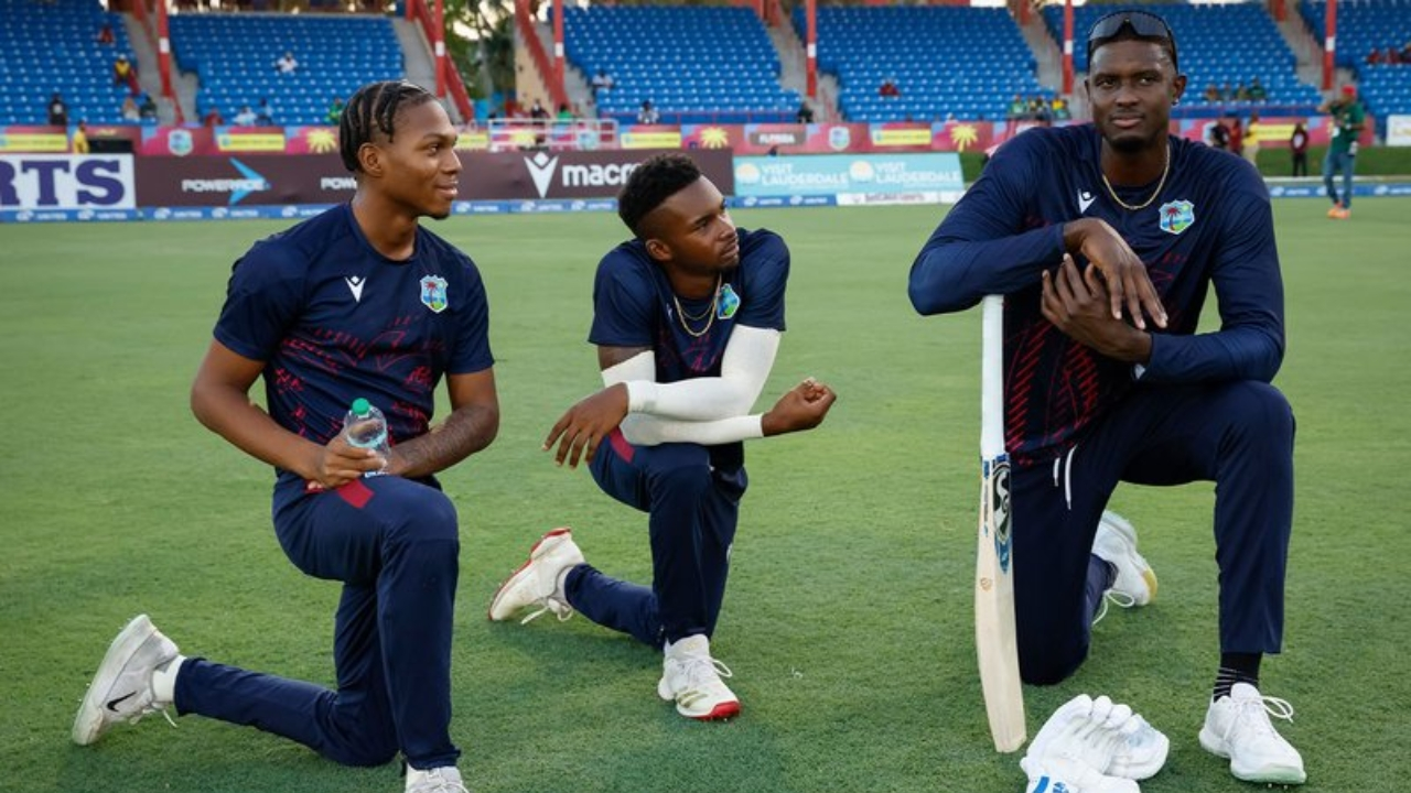 Jason Holder with two West Indies teammates kneeling on the field during a training session.