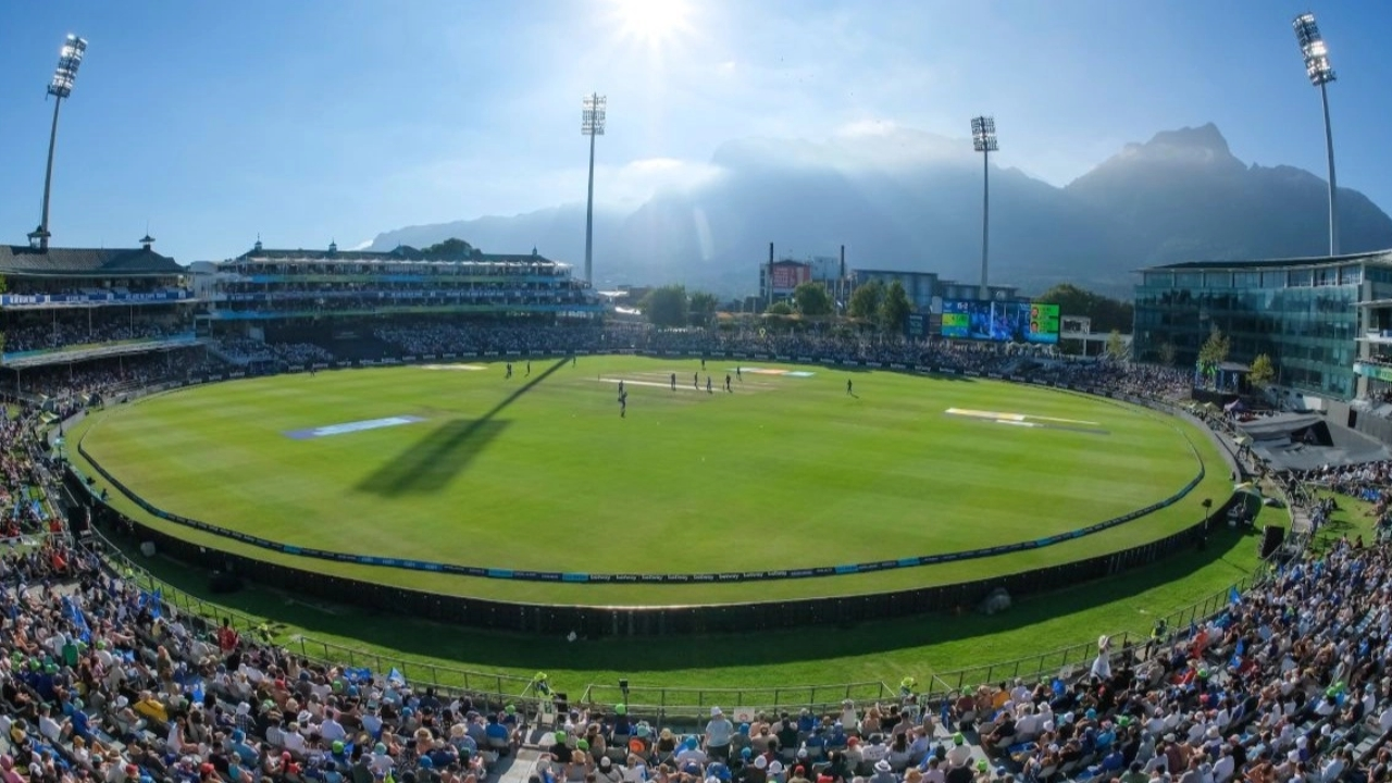 Panoramic view of Newlands Cricket Ground in Cape Town, South Africa, with a match in progress under bright sunlight and a full crowd in attendance.