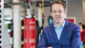 Pete Fitzboydon, sports executive, posing in a gym setting while wearing a blue suit and smiling at the camera.