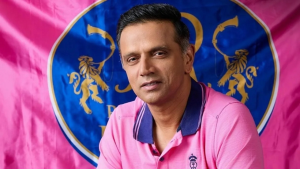 Rahul Dravid wearing a pink shirt with the Rajasthan Royals flag in the background.