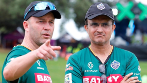 Sourav Ganguly and Jonathan Trott in team jerseys having an on-field discussion during a cricket event.
