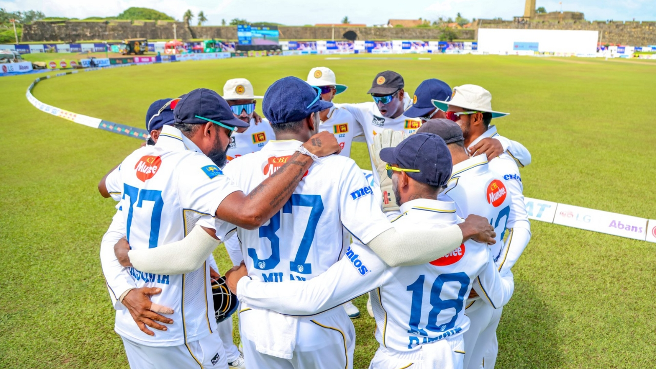 Sri Lanka national cricket team players in white Test kits forming a huddle on the field before a match.