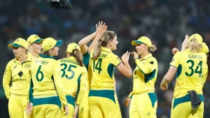 Australia women's cricket team players celebrate a wicket on the field wearing yellow and green uniforms during a match under lights.