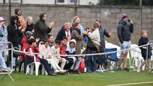 Parents and children cheering from the sidelines during a youth cricket match, showing community support and excitement