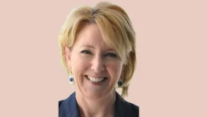 Portrait of Donna-Maria Cullen, executive at Tottenham Hotspur, smiling in a navy blazer with earrings against a light pink background.
