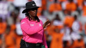 Jacquline Williams officiating as an ICC cricket umpire in a pink uniform during an international match.
