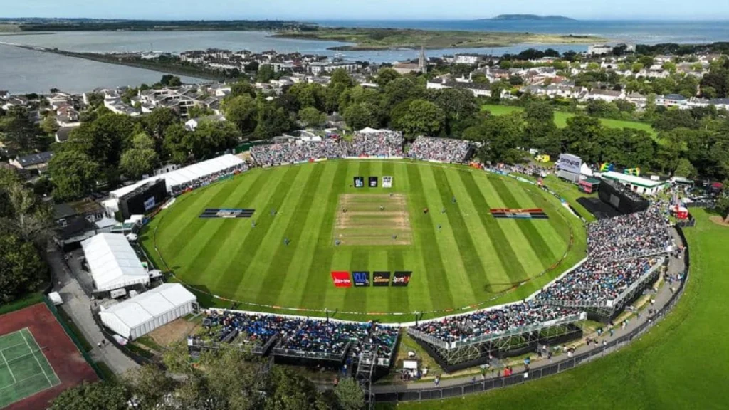 Aerial view of Malahide Cricket Ground in Dublin during a match, with full crowd and scenic coastal background.