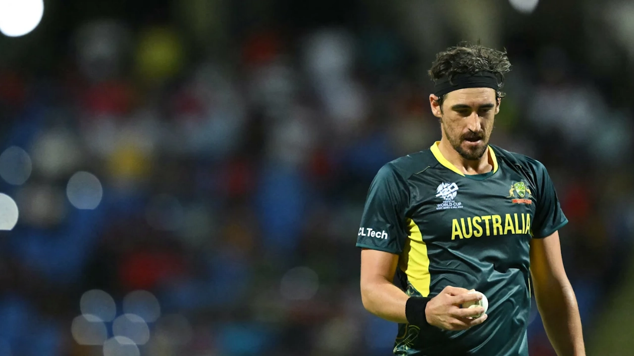Mitchell Starc holds the ball while preparing to bowl during a T20I World Cup match for Australia, wearing the national team's dark green jersey.
