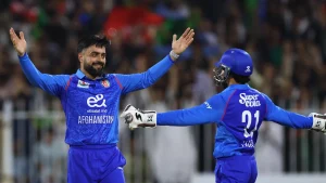 Rashid Khan celebrates with a teammate during an ODI cricket match for Afghanistan, wearing the national team's blue jersey.