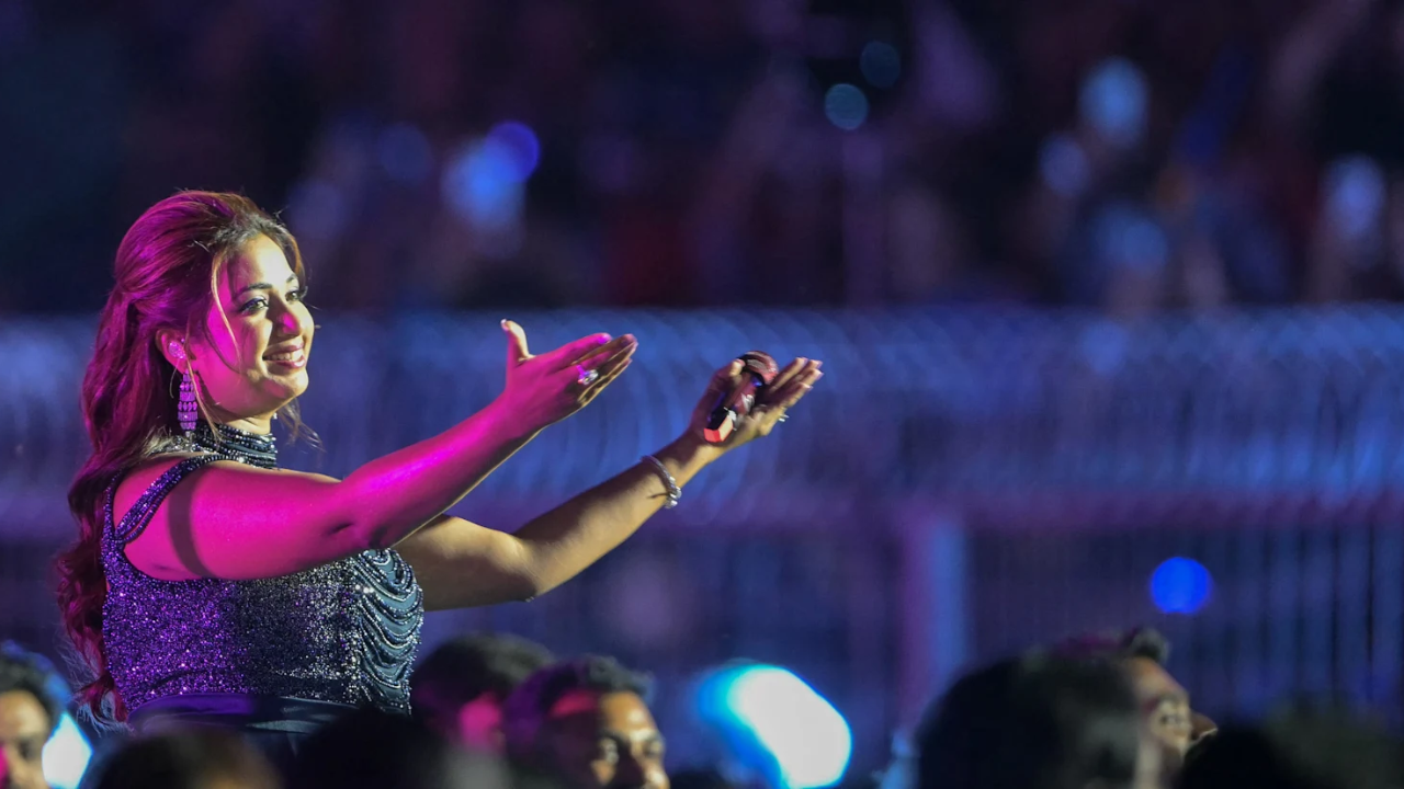 Indian playback singer Shreya Ghoshal performing live on stage, holding a microphone and engaging with the audience under concert lighting.