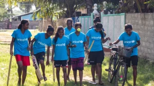 Group of Sri Lankan girls in UNICEF shirts playing cricket and walking with a bicycle during a community program