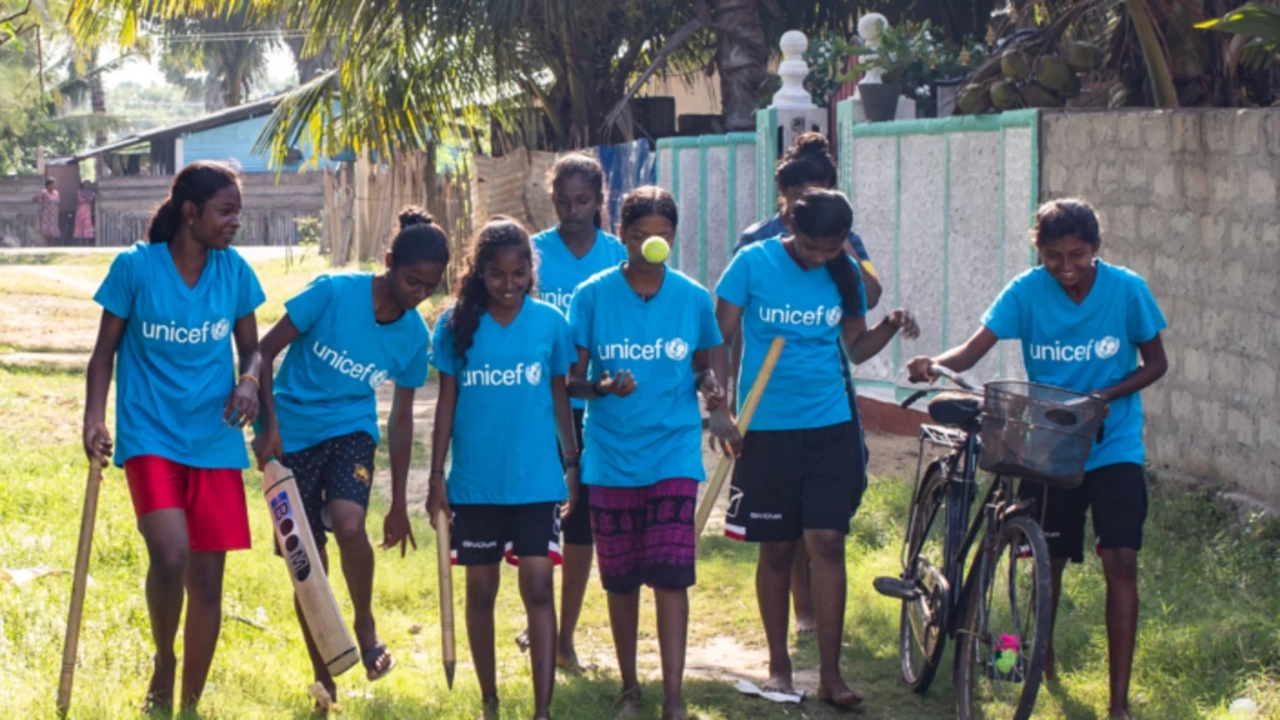 Group of Sri Lankan girls in UNICEF shirts playing cricket and walking with a bicycle during a community program